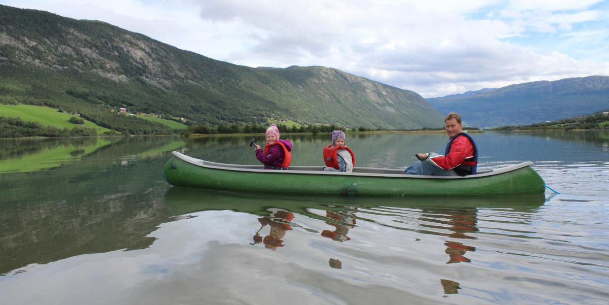 en voksen og to barn sitter i en kano på elven